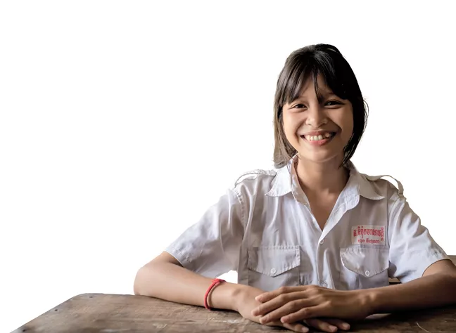 En ungdom sitter i en skolbänk. Hon ser glad ut. 